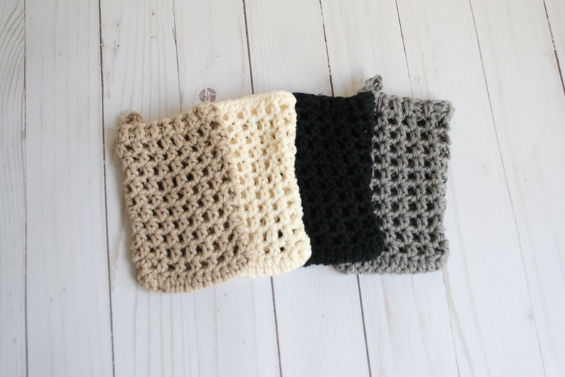 May include: Four crocheted dishcloths in beige, cream, black, and gray. The dishcloths are made with a simple open stitch pattern.