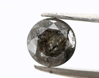 May include: A round, dark gray diamond with a faceted cut. The diamond is held in place by a pair of tweezers.