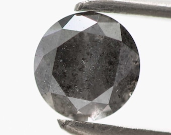 May include: A round, dark gray diamond with a faceted cut. The diamond is held by a pair of tweezers.