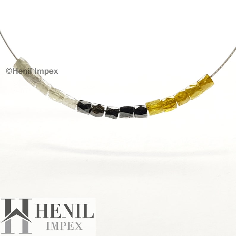May include: A strand of beads made from rough, uncut diamonds. The beads are arranged in a gradient pattern, starting with white, then black, and finally yellow. The beads are strung on a silver wire.