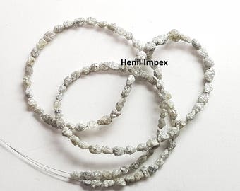 Könnte beinhalten: Eine Strähne aus rauen, grauen Diamantperlen. Die Perlen sind auf einem dünnen Draht aufgefädelt und in einem lockeren Kreis angeordnet. Der Text "Henil Impex" ist im Bild sichtbar.
