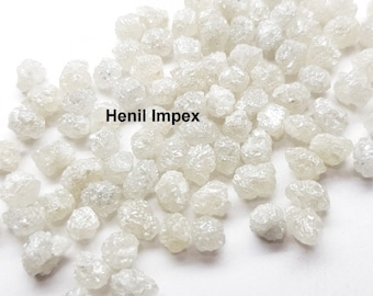 May include: A close-up of a pile of small, white, rough diamonds. The diamonds are scattered on a white surface. The text "Henil Impex" is visible in the image.
