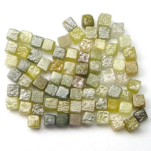 May include: A collection of small, square, faceted diamonds in various shades of green, yellow, and brown. The diamonds are arranged in a loose, random pattern.