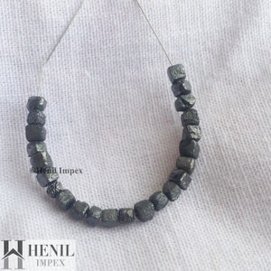 May include: A strand of black, faceted, square-shaped beads strung on a silver wire. The beads are all approximately the same size and have a rough, textured surface.