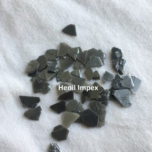 Peut inclure: Un tas de petites pièces en plastique gris foncé de forme irrégulière. Les pièces sont éparpillées sur une surface blanche. Le texte "Henil Impex" est visible sur l'image.