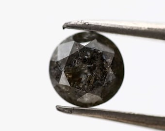 May include: A round, black diamond with a faceted cut. The diamond is held by tweezers and has a dark, cloudy appearance.
