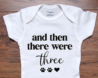 May include: White baby onesie with black text that reads "and then there were three" with two paw prints and a heart.