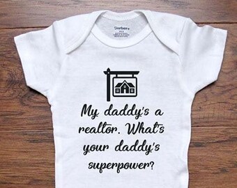 May include: White baby onesie with black text that reads "My daddy's a realtor. What's your daddy's superpower?"  A small black house icon is above the text.