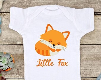 May include: White baby onesie with a cartoon orange fox sleeping on it. The onesie has the text "Little Fox" printed on it.