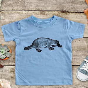 May include: A light blue t-shirt with a black and white illustration of a platypus on the front.