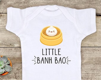 May include: White baby onesie with a cartoon illustration of a steamed bun with a smiling face. The text "LITTLE BANH BAO" is printed below the illustration.
