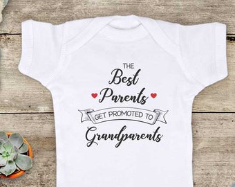 May include: White baby onesie with black text that reads "The Best Parents Get Promoted To Grandparents". The text is surrounded by a banner and two red hearts.
