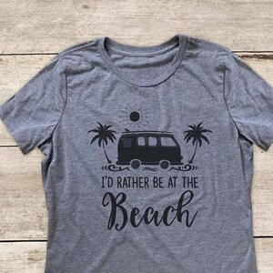 May include: Gray t-shirt with a black graphic of a vintage van with a surfboard on top, palm trees, and a sun. The text "I'd rather be at the Beach" is printed below the graphic.