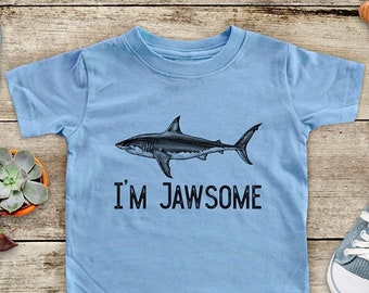 May include: A light blue t-shirt with a black and white shark graphic and the text "I'm Jawsome".