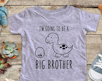 May include: A gray short-sleeved t-shirt with a black dinosaur graphic and the text "I'm going to be a big brother".