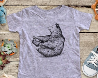 May include: A heather grey t-shirt with a black and white illustration of a bear sitting in a yoga pose.