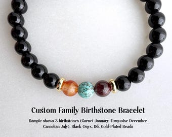 May include: A black onyx bracelet with three colorful birthstones and gold-plated beads. The bracelet features a garnet, turquoise, and carnelian stone. The text reads "Custom Family Birthstone Bracelet."