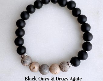 May include: A black onyx and druzy agate bracelet. The bracelet features round, matte black onyx beads and a series of gray and tan druzy agate beads. The text at the bottom reads "Black Onyx & Druzy Agate" and "8mm, Real Platinum-Plated Spacer Beads."