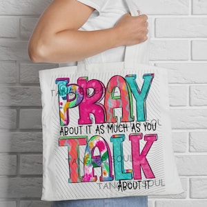Puede incluir: Una bolsa de tela blanca con un diseño gráfico colorido que incluye el texto PRAY ABOUT IT AS MUCH AS YOU TALK ABOUT IT. Las letras están rellenas con patrones vibrantes en rosa, turquesa y motivos florales, sobre un fondo de líneas negras finas.