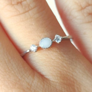 May include: A silver ring with three white stones. The center stone is round and the two smaller stones are on either side.