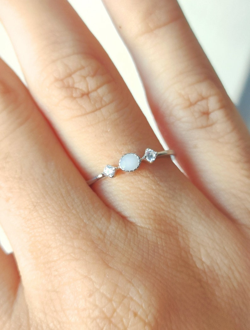 May include: A silver ring with three white stones. The center stone is round and the two smaller stones are on either side.