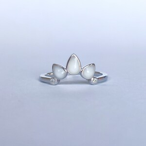 May include: A silver ring with three white teardrop-shaped stones and two small clear stones.