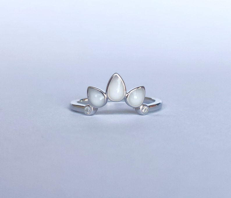 May include: A silver ring with three white teardrop-shaped stones and two small clear stones.