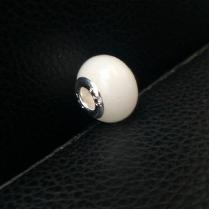 May include: White ceramic bead with a silver metal band around the center. The bead is smooth and glossy.