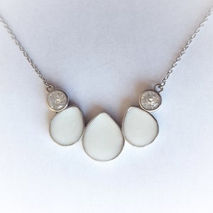 May include: A silver necklace with three white teardrop-shaped pendants and two clear round stones.
