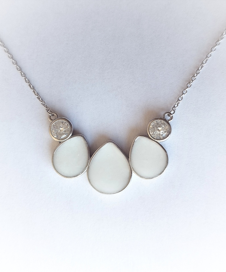May include: A silver necklace with three white teardrop-shaped pendants and two clear round stones.