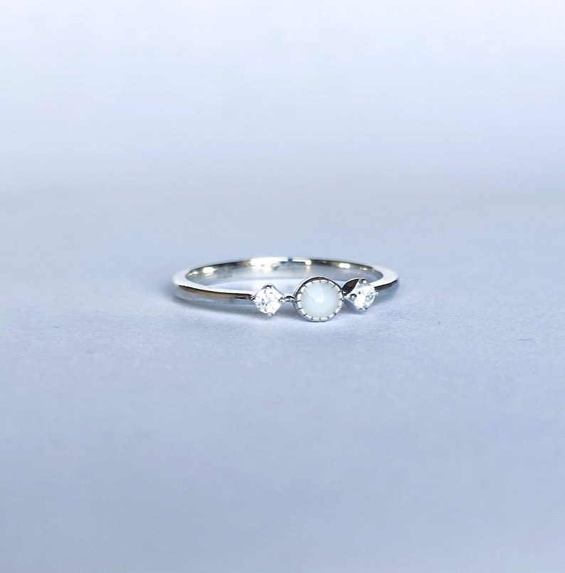May include: A silver ring with three white stones. The center stone is round and the two side stones are square.