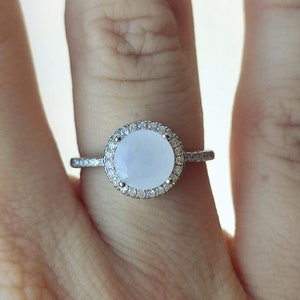 May include: A silver ring featuring a large, oval-shaped, white gemstone encircled by a halo of smaller, clear gemstones.