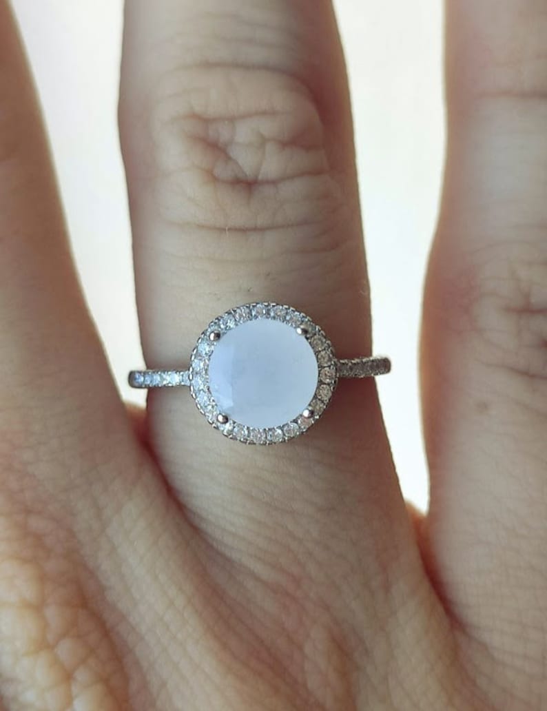 May include: A silver ring featuring a large, oval-shaped, white gemstone encircled by a halo of smaller, clear gemstones.