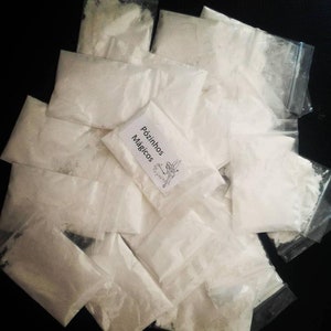 May include: A pile of small white bags with a label that reads "Pózinho Mágicos" on one of the bags. The bags are made of clear plastic and are filled with a white powder.
