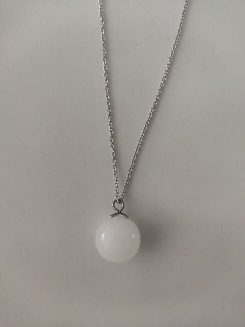 May include: A silver chain necklace with a white orb pendant.