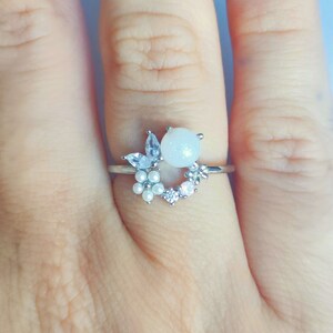 以下が含まれることがあります： 白い真珠と透明なクリスタルが花柄にデザインされたシルバーリングです。