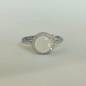 May include: A silver ring featuring a white gemstone set in a halo of smaller white gemstones.