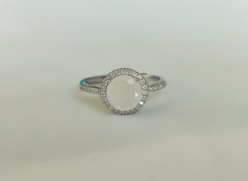May include: A silver ring featuring a white gemstone set in a halo of smaller white gemstones.