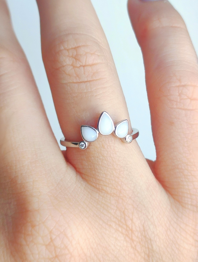 May include: A silver ring with three white teardrop-shaped stones and two smaller clear stones.