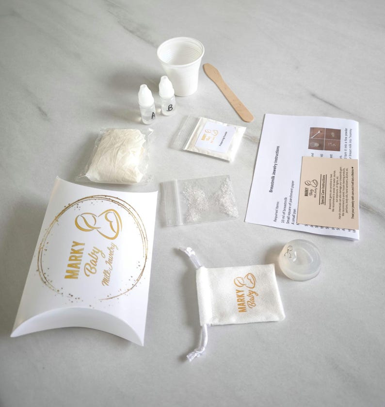 May include: A kit for making resin jewelry, including a white bag of resin, two small bottles of liquid, a small bag of glitter, a white cup, a wooden stick, a small bag of white powder, a white pouch with a gold logo that says "Marky Baby Milk Jewelry", a white bag with a gold logo that says "Marky Baby", and a clear resin mold in the shape of a heart.