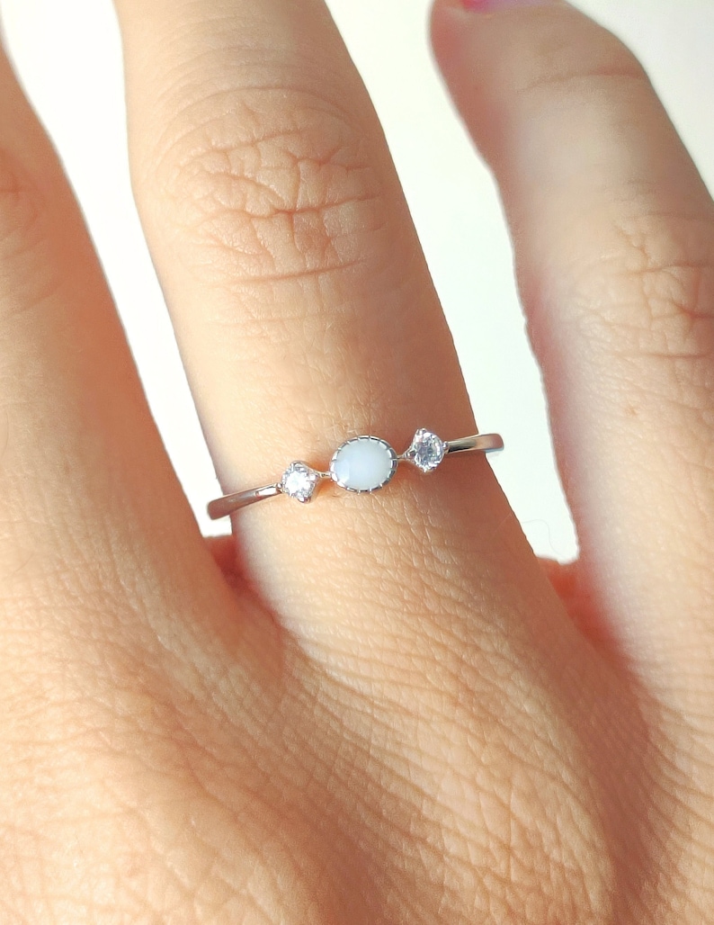 May include: A silver ring with three white stones. The center stone is larger and oval-shaped, while the two smaller stones are round.