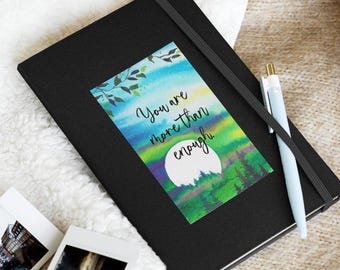 May include: A black journal with a watercolor design featuring a moon, trees, and the text "You are more than enough".