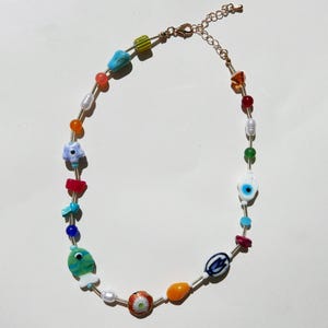 May include: A colorful beaded necklace with a gold-tone chain. The necklace features a variety of beads, including pearls, flowers, and eye-shaped beads. The beads are in shades of blue, green, red, orange, and white.