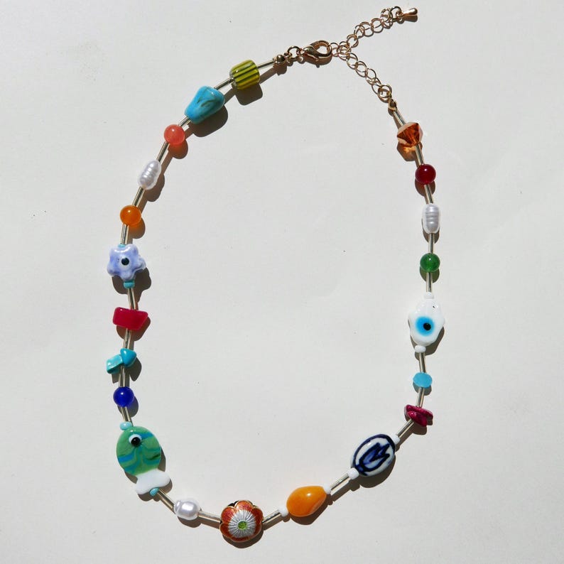 May include: A colorful beaded necklace with a gold-tone chain. The necklace features a variety of beads, including pearls, flowers, and eye-shaped beads. The beads are in shades of blue, green, red, orange, and white.
