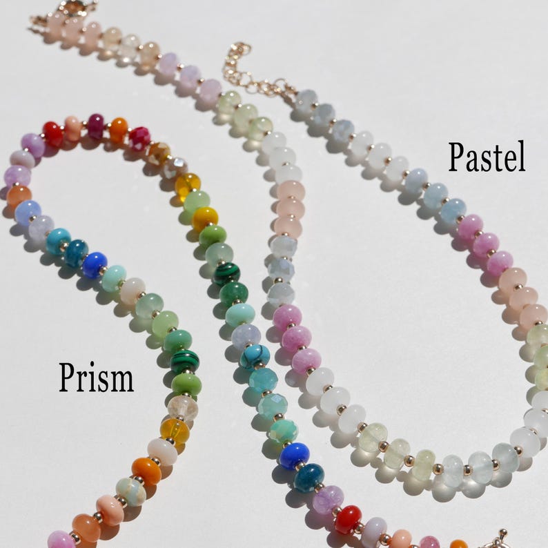 May include: Close-up of three beaded necklaces in various colors. One necklace is labeled "Prism" and features a rainbow of colors. Another is labeled "Pastel" with soft, light colors. The third necklace is a light pink color.