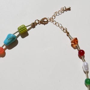May include: A colorful beaded necklace with a gold-tone chain and clasp. The necklace features a variety of beads in shades of green, blue, orange, red, and white. The beads are strung on a thin wire.