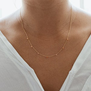 May include: A delicate gold chain necklace with small pink beads hanging from it.