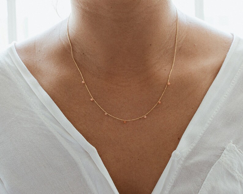 May include: A delicate gold chain necklace with small pink beads hanging from it.