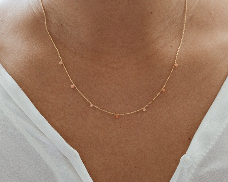 May include: A delicate gold chain necklace with small, light pink beads hanging from it.