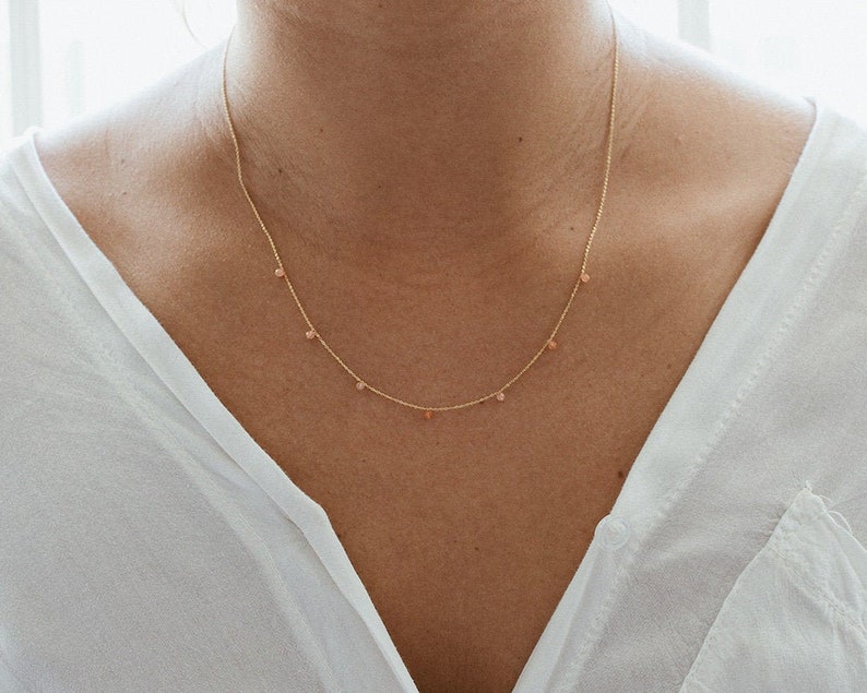 May include: A delicate gold chain necklace with small, light pink gemstone accents.